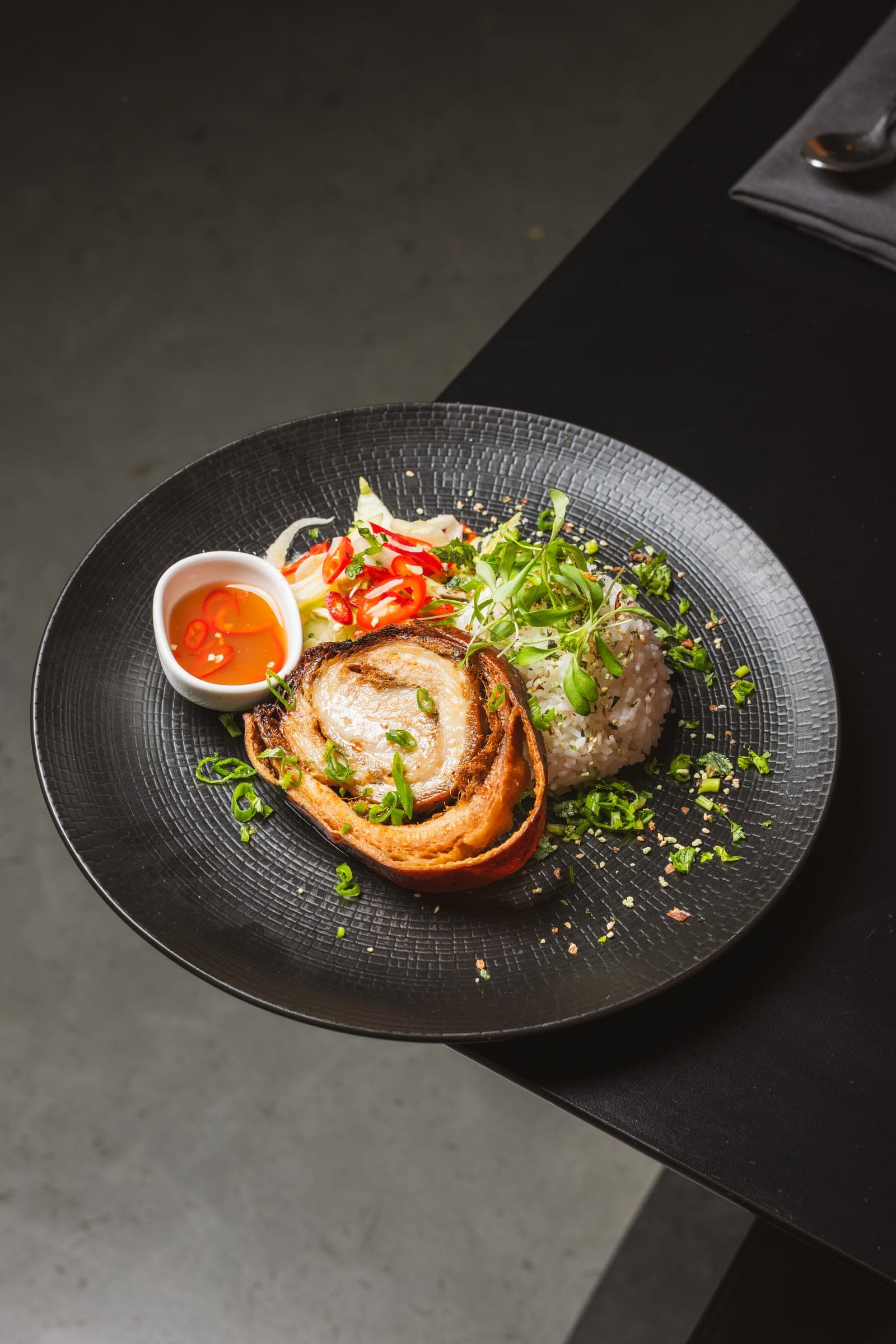 Porchetta roll plated with chili on charcoal ceramic