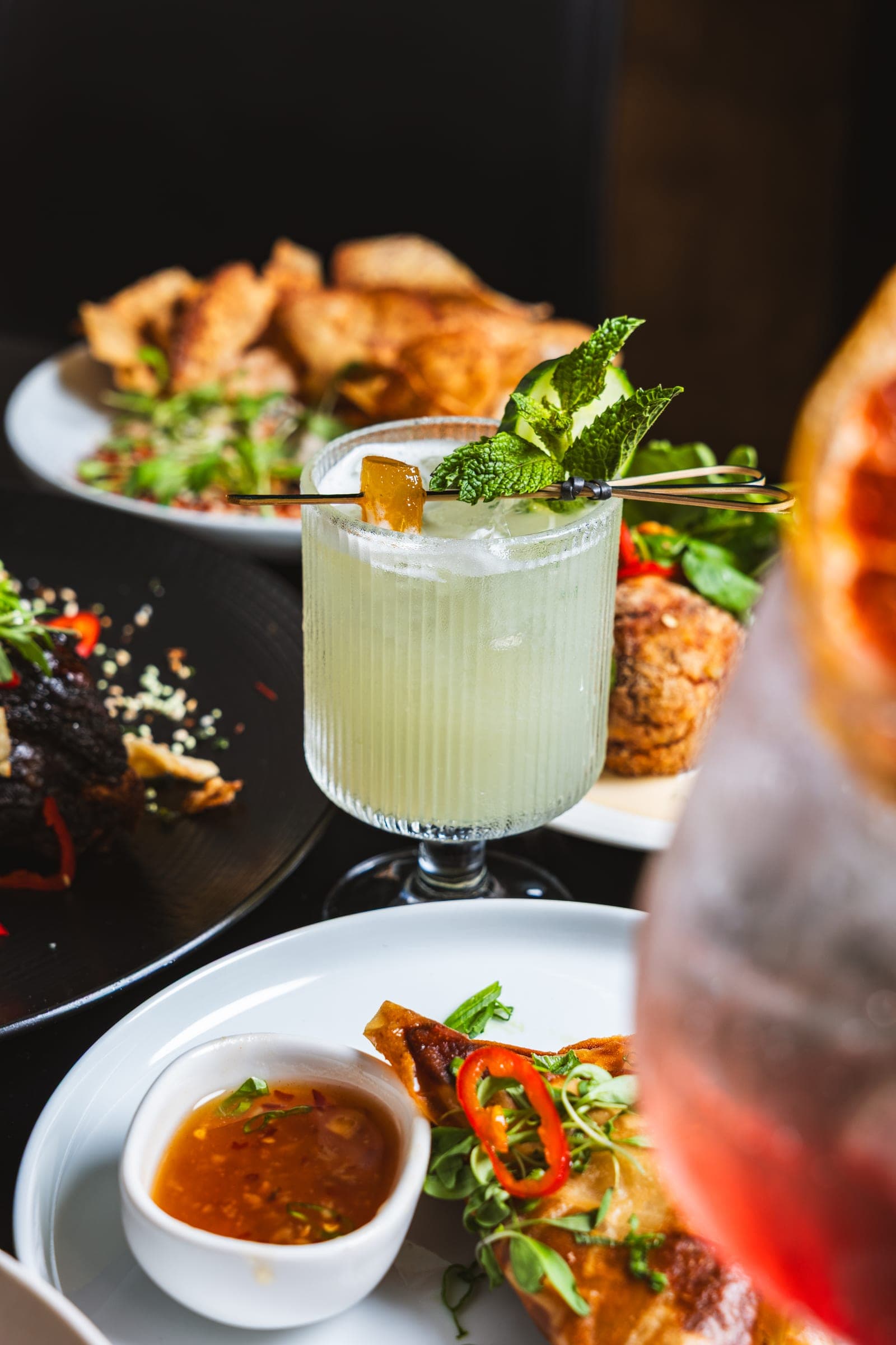 Bright green cocktail beside shared plates